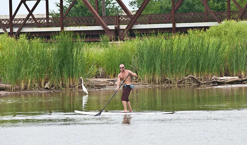 Eric Pappas mingles with wildlife as he demonstrates surf paddle board technique on the waterway connecting Stinchcomb Wildlife Refuge and Lake Overholser as it passed under the old Route 66 Bridge, Background. - MARK HANCOCK