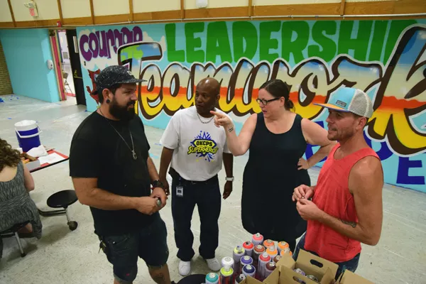 Left to right, Sean Vali, Warren Pete, school principal, Romy Owens, and Jason Pawley discuss murals on the cafeteria walls at F.D. Moon Elementary School, 1901 N.E. 13th Street in Oklahoma City, during the mural painting project, 7-14-16. - MARK HANCOCK