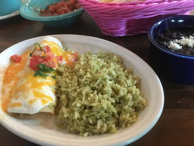 A lunch chicken enchilada topped with sour cream sauce and served with green rice and refried black beans - JACOB THREADGILL