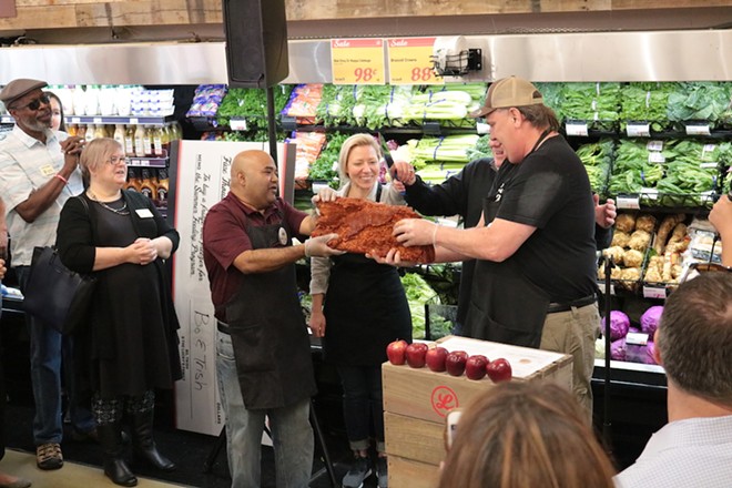 David Maloo (Assistant Store Director), Trish and Bo Sharon (owners), and Bob Knaus  (Store Director) cut house-cured bacon instead of a ribbon to celebrate the opening of Lucky’s Market - PHOTO COURTESY LUCKY’S MARKET