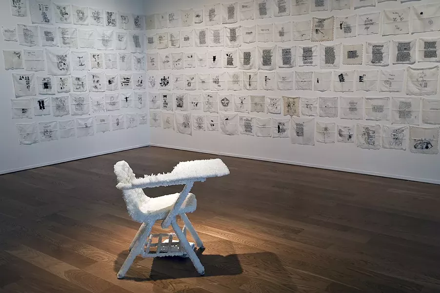 “Love Letters/White Flag: The Book of God” by Noelle Mason, 2009-2016, - hand-embroidered white handkerchiefs. “Through a glass, darkly (spring cleaning)” by Noelle Mason, 2016, Borax, combo desk, composition notebook, No. 2 pencil
