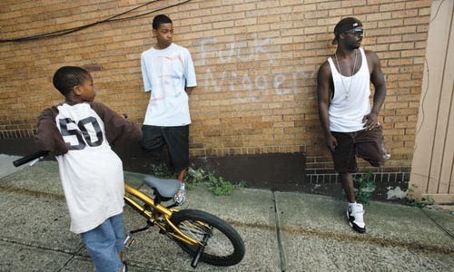 A child passes by as Shiquan Jones (left) and his uncle Troy Jones lean against a building spray-painted with a racial slur. - HEATHER MULL