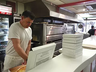 Aiello's employee Tim Watts cuts slices of Aiello's pizza for customers mourning the passing of owner Joe Aiello. - PHOTO BY AMYJO BROWN