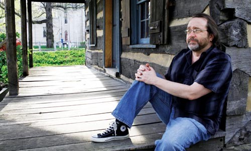 Around my cabin door: Martin Giles sits on the porch of a cabin on the University of Pittsburgh campus; in the background is visible the Stephen Foster Memorial, where his new play Beautiful Dreamers will be staged. - HEATHER MULL