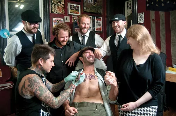 Band members Ben Jaber, Danny Rectenwald, Dan Stocker, Jon Pitcher and Rachel Karras watch as tattoo artist Justun Palencssar works on singer Jimmy Bastard - PHOTO BY CAROLINE MOORE