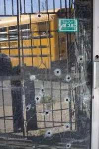 The reflection of an afternoon schoolbus passing by, showin in the bullet-hole riddled door of a vacant bar on the corner of Lincoln Avenue and Rowan Street in District 9 - HEATHER MULL