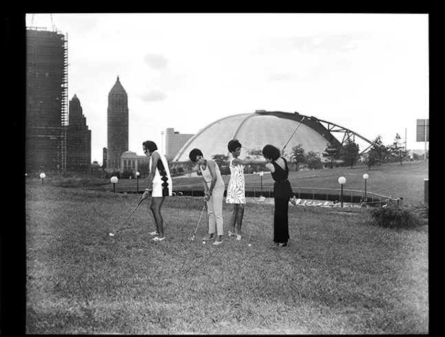 Lynette May, Gerri Walker, Shirley Jenkins, and Alberts Thompson hitting golf balls at Washington Plaza putting field with Civic Arena in the background, 1969 - TEENIE HARRIS
