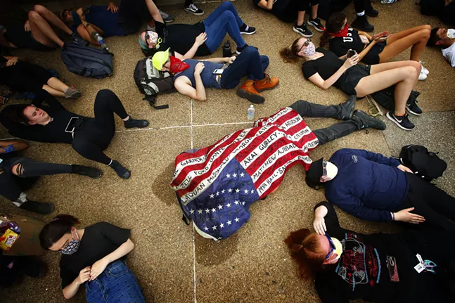 A protester underneath an American flag outside of the Allegheny County Jail with the names of Black people whose lives were lost at the hands of police. - CP PHOTO: JARED WICKERHAM