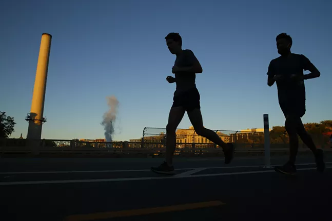 Students run across Schenley Bridge as the sun sets over the Carnegie Mellon University campus in the background. - CP PHOTO: JARED WICKERHAM