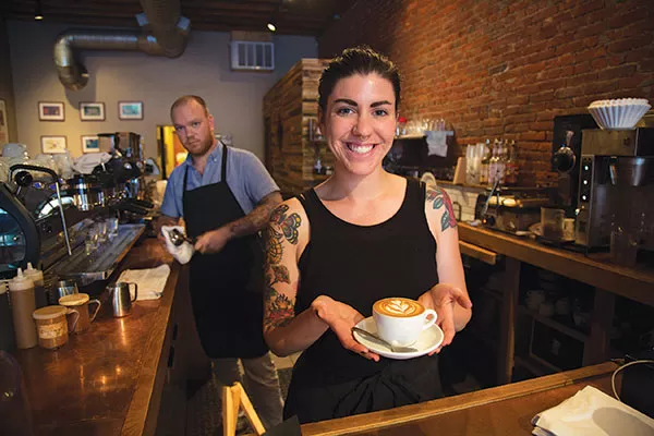 Emily Hurley shows off a caffeinated work of art made by Braden Walter Jr. (background). - PHOTO BY THEO SWARTZ