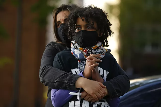 Holly Hickling holds her daughter, Nzinzi Tembo, as protesters speak before marching from Freedom Corner. - CP PHOTO: JARED WICKERHAM