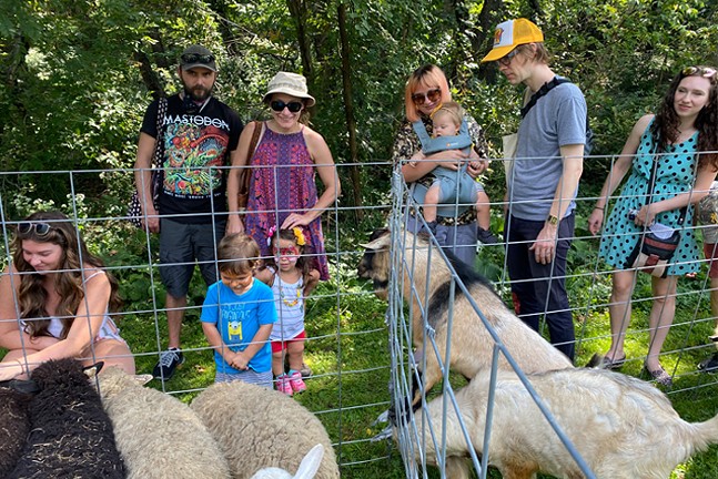A group of men, women, and children stand at a fence petting goats and sheep.