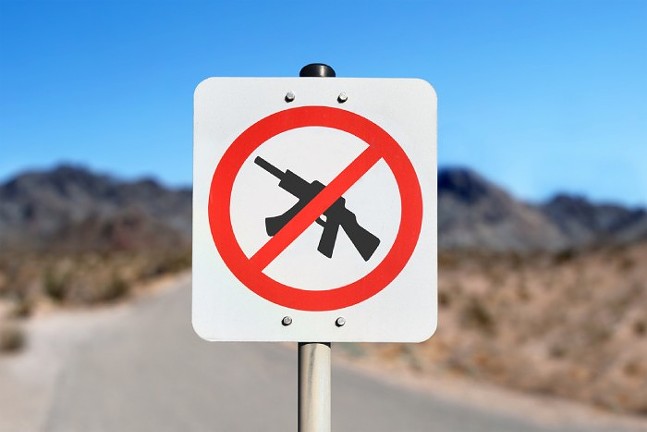 A "no weapons" road sign, with a black silhouette of a large gun crossed out by a red line and circle
