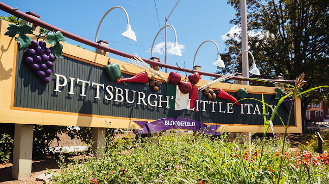 Un cartel rodeado de vegetación dice "Little Italy Bloomfield de Pittsburgh."
