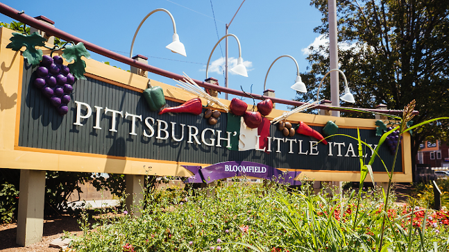 Un segno circondato da piante che legge "La piccola Italia Bloomfield Pittsburgh."