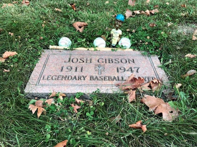 A grave marker that says "Josh Gibson 1911-1947 Legendary Baseball Player) surrounded with baseballs and a baseball figurine