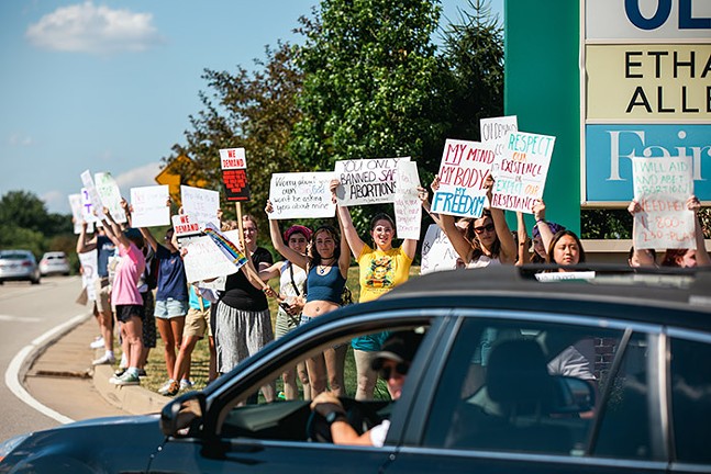 A row of young women hold up pro-abortion rights signs to a passing car