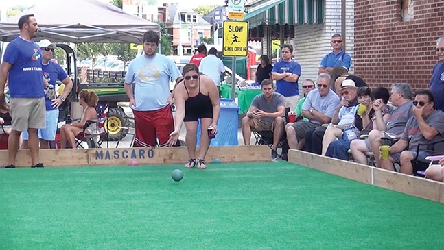 A crowd watches as a woman throws a green bocce ball onto a court