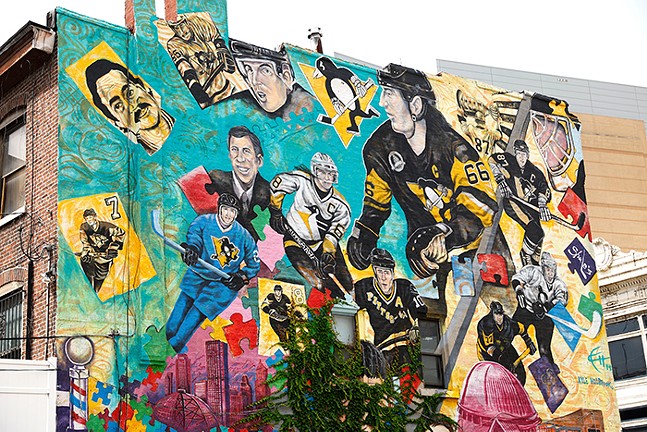 A colorful mural painted with collages of hockey players, a penguin mascot, and puzzle pieces