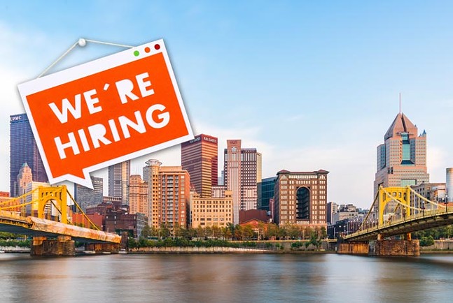 A sign that says "We're Hiring" is placed on top of a photograph of a Downtown city skyline and river
