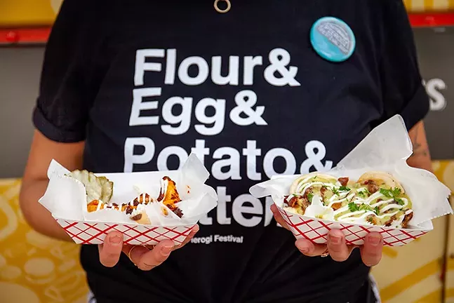 A person shot from below the neck holds two containers of loaded pierogis.
