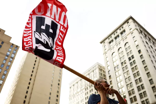 A person holds up a flag that says "organize" and "union" in front of tall city buildings
