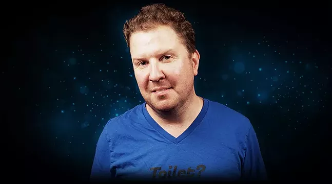 A man smiles in front of a dark sky background and wearing a shirt that says "Toilet?"
