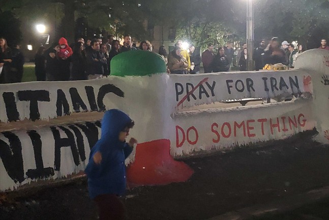 Members of Pittsburgh's Iranian community stand behind a banner that reads Pray for Iran, with the word "pray" crossed out and, underneath, another banner that reads "Do Something."