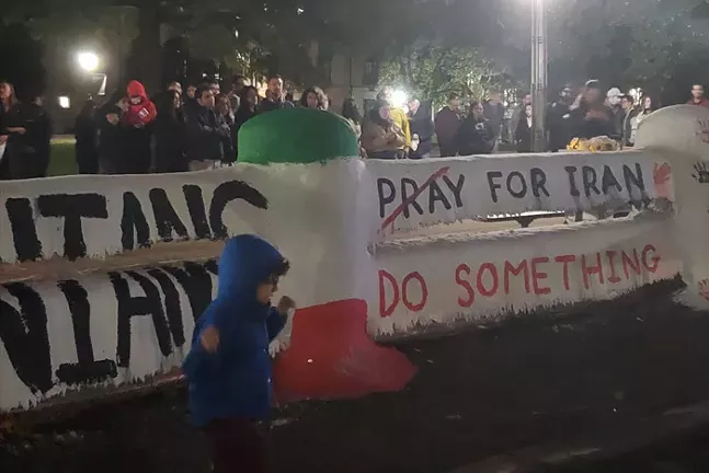 Members of Pittsburgh's Iranian community stand behind a banner that reads Pray for Iran, with the word "pray" crossed out and, underneath, another banner that reads "Do Something."