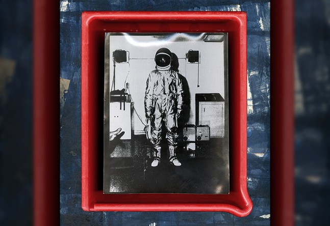 A photograph depicts a person in a spacesuit framed by red neon.