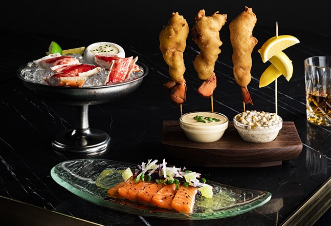 A variety of seafood is artfully presented on skewers, on a plate, and in a cocktail glass.