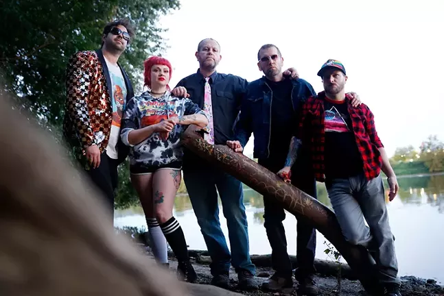 Five people stand together on the bank of a river