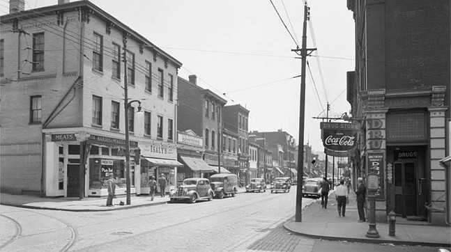 Black-and-white photo of a business street with reto cars and old signs.