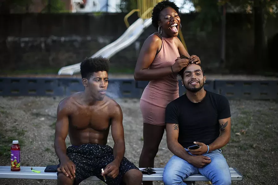 Keara Jordan does the hair of Angel Rodriguez while friends look on and play basketball at Sullivan Playground. - CP PHOTO: JARED WICKERHAM