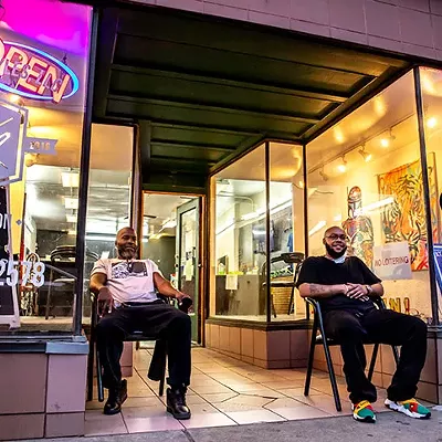 Barbers Bobby Fletcher and Brandon Potts watch the action on East Carson Street from outside unisex salon Trending Styles in Pittsburgh's South Side on Sat., April 10, 2021.