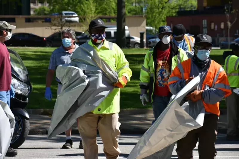 City workers with trash bags head into one of the tent cities on Friday. - DOYLE MURPHY