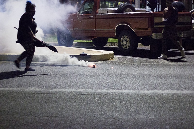 A protester prepares to kick a tear gas canister back to the police line. - PHOTO BY DANNY WICENTOWSKI