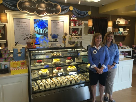 Twin sisters Jannette Neely (right) and Penelope Ritchie (left) stand in front of the bundt cake show case inside of their Nothing Bundt Cake franchise in Town and Country, Missouri. - EMILY MCCARTER