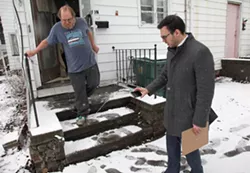 Wayne Russell, who is Linda Barger's brother, points out their landlord's attempt at fixing their front porch, while Mike Furlano, an attorney with the Legal Aid Society of Rochester, photographs it. - PHOTO BY MAX SCHULTE