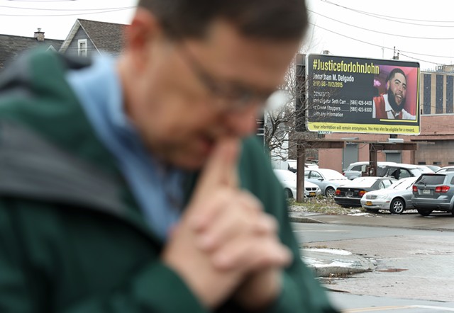 Ed Knauf prays at the corner of North Clinton Avenue and Norton Street in December 2021 for homicide victim Christopher Porchea, 51. Across the street stood a billboard seeking information in the killing of Jonathan Delgado, who was murdered in 2015. - PHOTO BY MAX SCHULTE