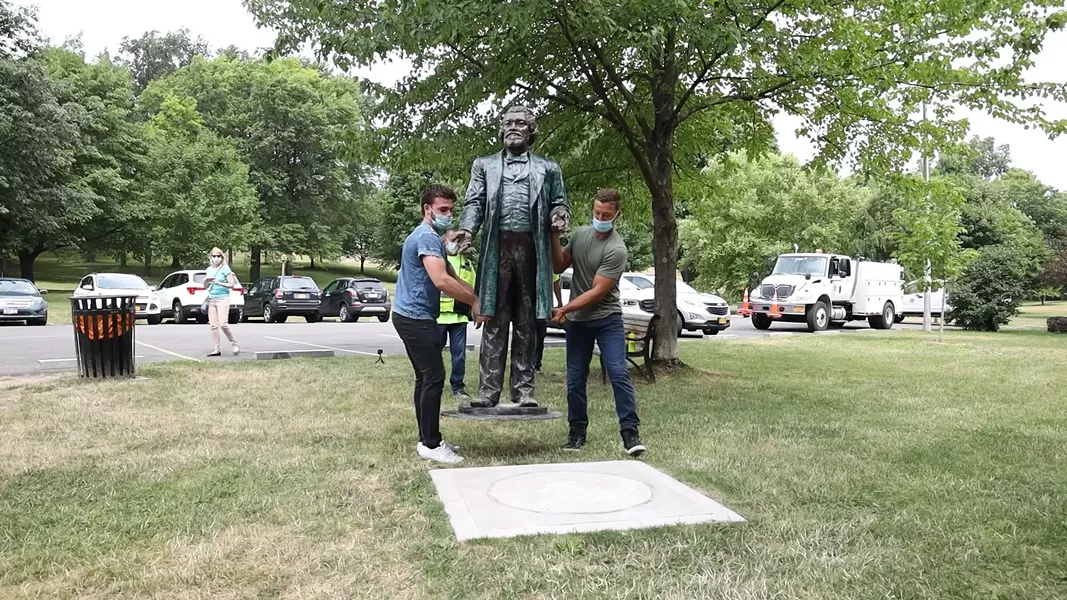 John Boedicker, left, and Charles Milks carry a Frederick Douglass statute made by sculptor Olivia Kim to its base at Kelsey's Landing in Maplewood Park. - PHOTO BY MAX SCHULTE