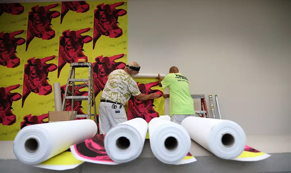 Workers at the Memorial Art Gallery hang cow wallpaper that is part of the "Season of Warhol" exhibit. - PHOTO BY MAX SCHULTE