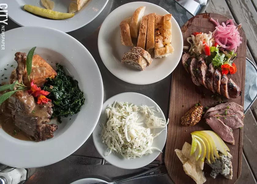 A recent lunch special at Stonecat Cafe: Bone-in braised duck leg served with sautéed kale and a savory sage biscuit (left). Also pictured: house-made bread, cole slaw, and charcuterie board. - PHOTO BY REBECCA RAFFERTY