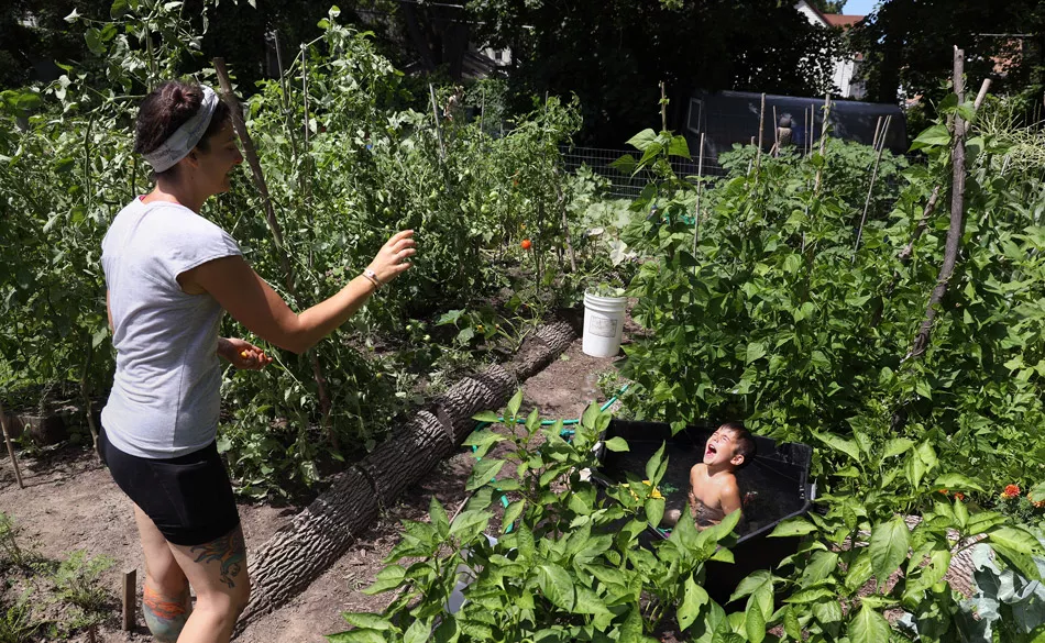 Sarah Spano, who lives on Exchange Street, tosses a sungold tomato from her garden to her son, Arlo. - PHOTO BY MAX SCHULTE