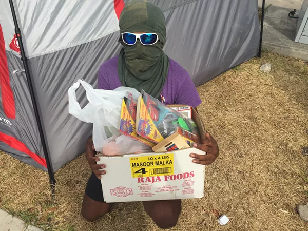 Occupy ICE San Antonio spokesman “Kazi” shows off a box of food and activity books the group gives out to people entering San Antonio’s ICE detention facility. - SANFORD NOWLIN