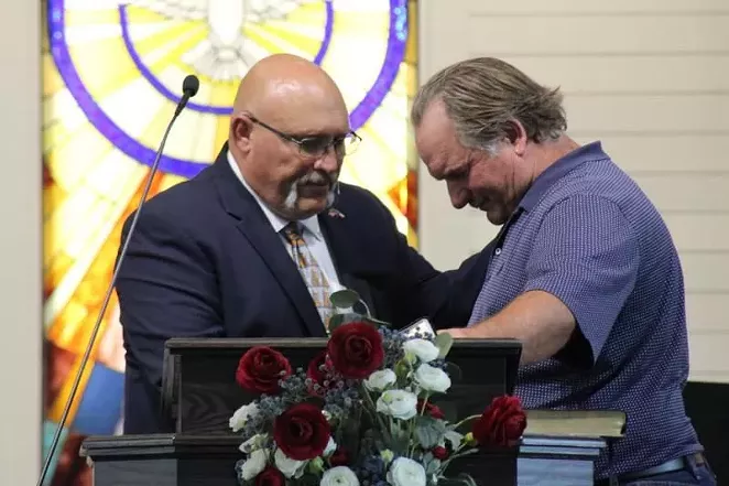 Frank Pomeroy (left) prays with a congregant. - TWITTER / @KERANEWS