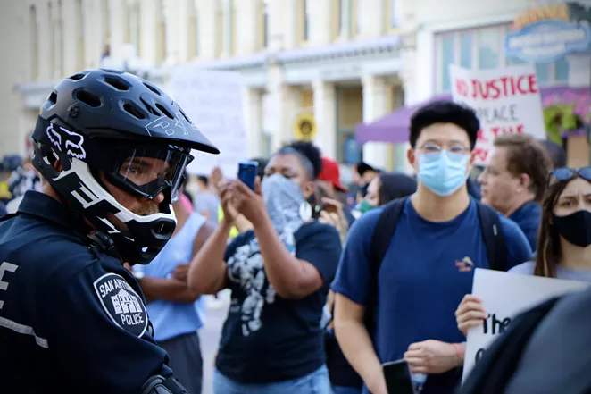 Protesters march by a San Antonio police officer at a demonstration last spring. - JAMES DOBBINS