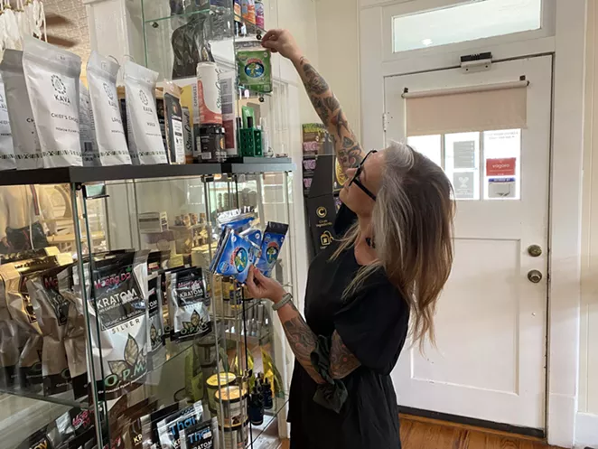 An employee at San Antonio CBD shop Mr. Farmacist removes Delta-8 gummies from a display case. - SANFORD NOWLIN