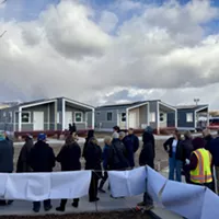 Attendees at a ribbon-cutting event pass by a row of tiny homes at The Other Side Village on Monday, Dec. 30, 2024.