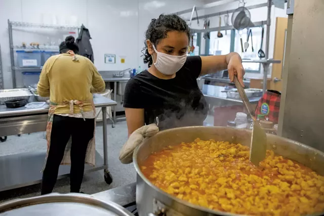 Haydee Miranda of Burlington (right) stirring a pot of curry chicken as Mulu Tewelde prepares more food for a takeout dinner - DARIA BISHOP